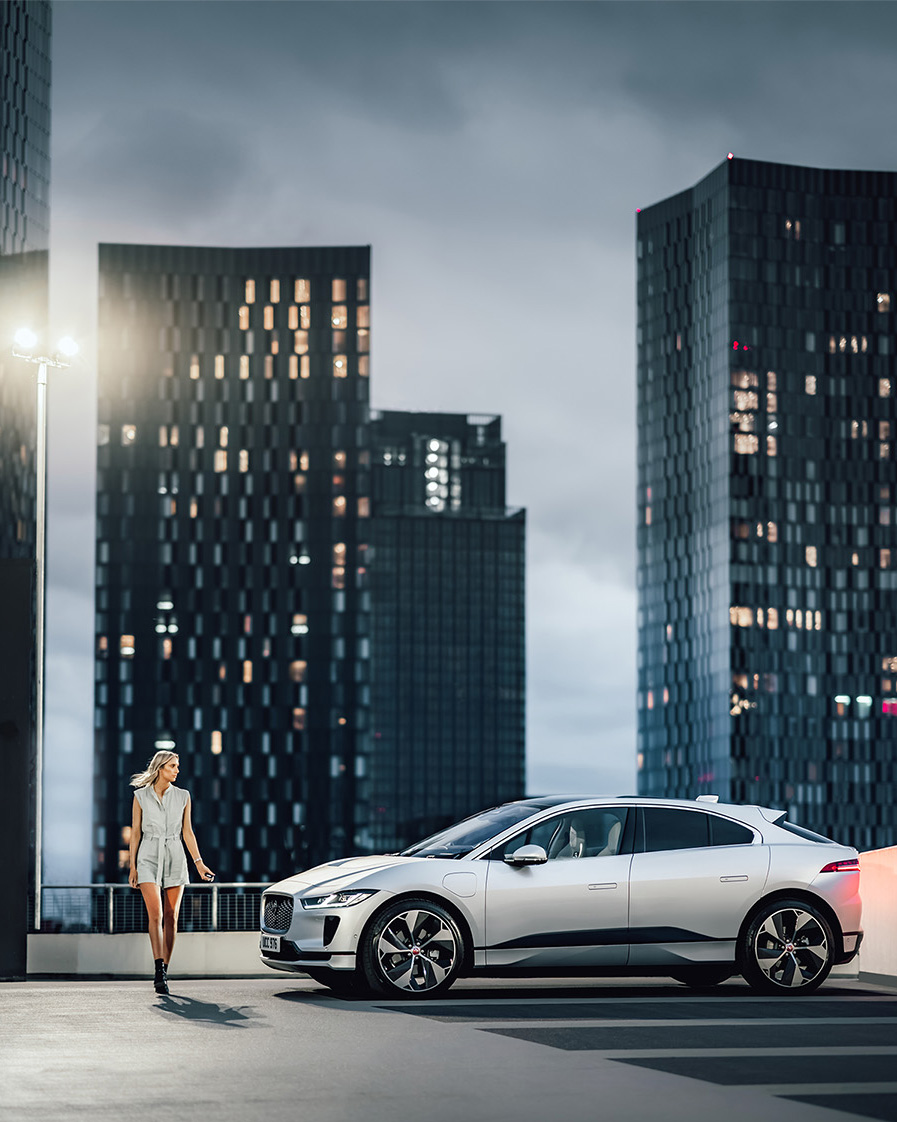 Woman in front of parked Jaguar with buildings in the background