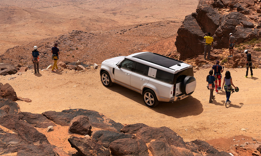 Land Rover on desert cliff with people walking around